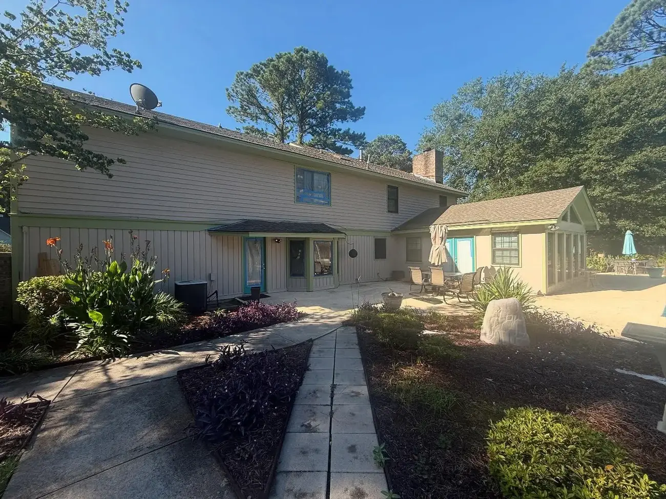 Rear exterior of a home freshly painted in cream and sage green, with a pool and patio